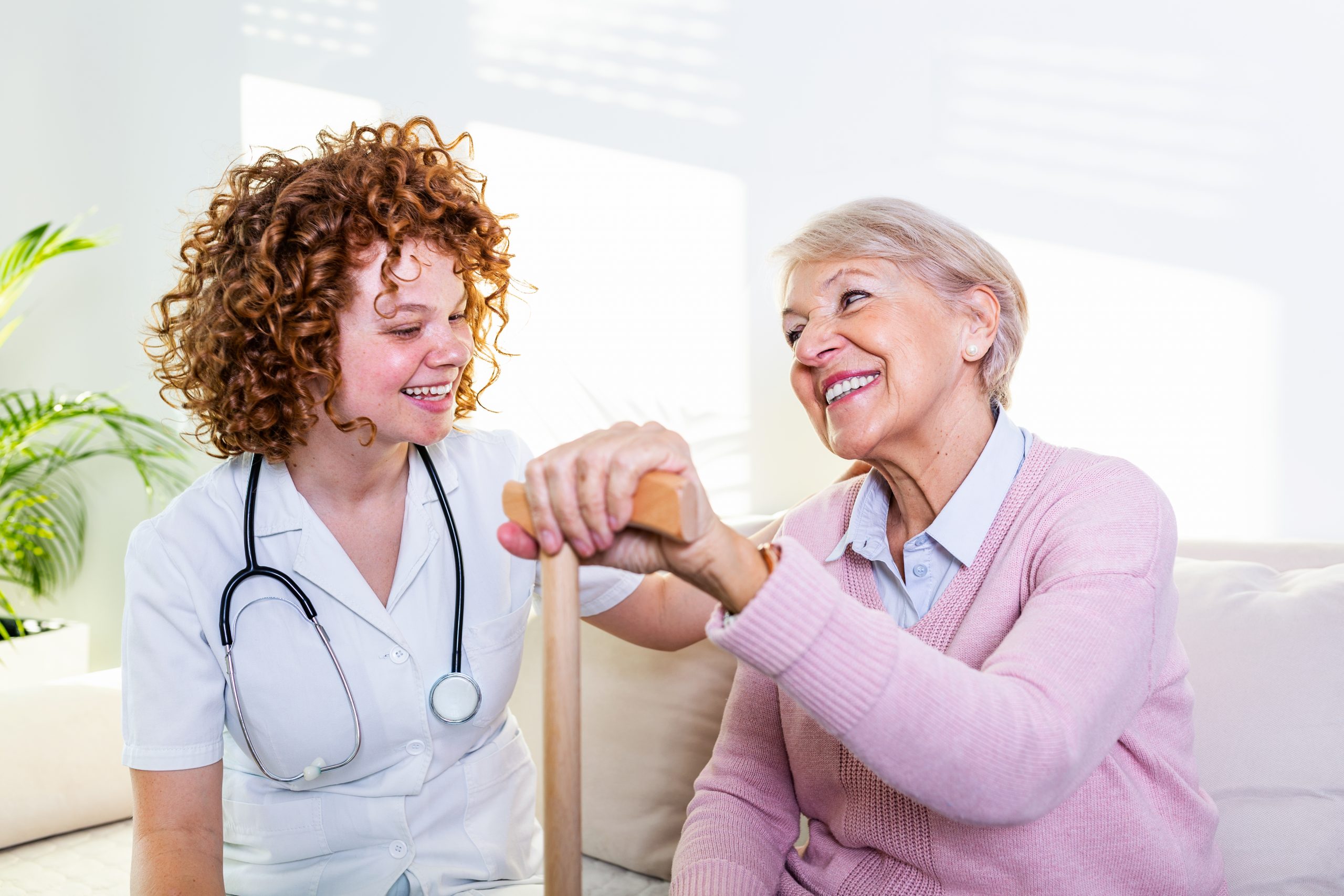 Young caregiver and senior woman laughing together while sitting on sofa. Senior woman and younger friend having fun together during meeting at home.